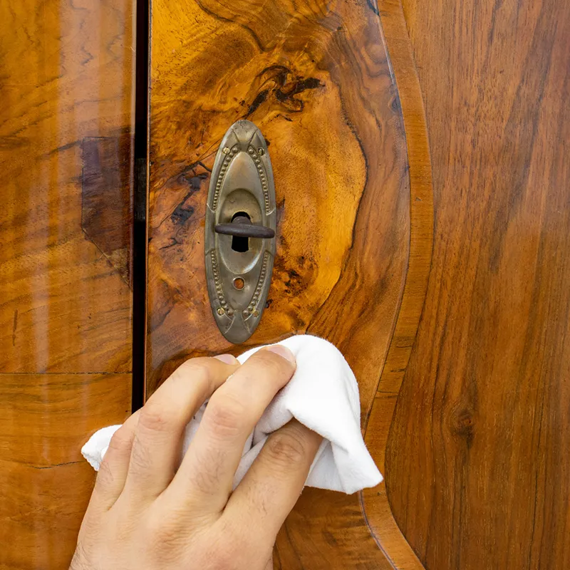 Eine Hand, die mit einem weißen Tuch einen antiken Holzschrank pflegt