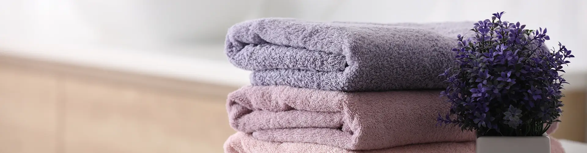 Saubere lilafarbene Handtücher vor einem verschwommenen Badezimmer-Hintergrund